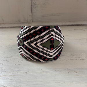May include: A black, white, and green headband with a geometric pattern. The pattern features red arrows and white crosses.
