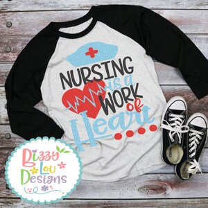 May include: A white and black baseball tee shirt with a blue and red graphic that says "Nursing is a work of heart".