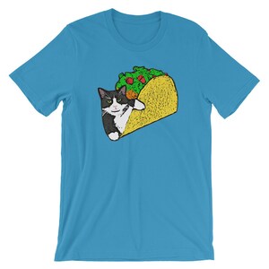 May include: A turquoise blue t-shirt with a black and white cat inside a yellow taco. The cat is looking at the viewer with a serious expression.