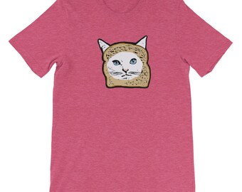 May include: A pink heather t-shirt with a white cat wearing a slice of bread on its head. The cat has blue eyes and a white face.