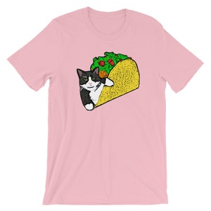 May include: A pink t-shirt with a black and white cat inside a yellow taco. The cat has a white patch on its chest and a black nose.