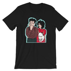 May include: A black t-shirt with a graphic of two people, a man and a woman, standing next to each other. The man is wearing a patterned shirt and the woman is wearing a red shirt. The woman is holding a white mask with red accents.