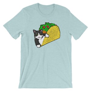 May include: A light blue t-shirt with a black and white cat in a yellow taco. The cat is looking at the viewer with a serious expression.