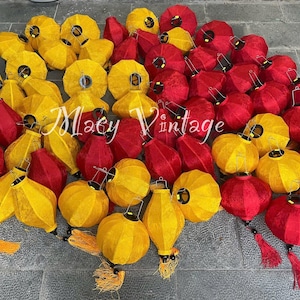 May include: A collection of red and yellow paper lanterns, some with tassels. The lanterns are arranged in a semi-circle on a gray surface.