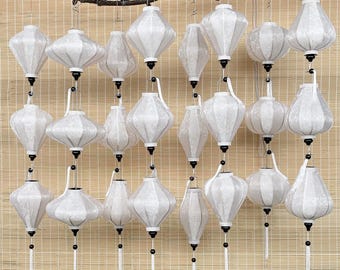 May include: A collection of 24 white paper lanterns hanging from a branch. The lanterns are all the same size and shape, and they are all decorated with a white tassel.