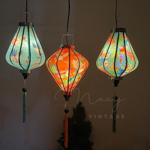 May include: Three hanging paper lanterns with different designs. The lanterns are made of silk and have a traditional Chinese style. The lanterns are lit and glowing.