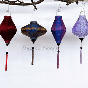 May include: Four silk lanterns hanging from a branch. The lanterns are red, blue, gold, and purple. Each lantern has a tassel hanging from the bottom.