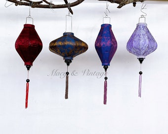 May include: Four silk lanterns hanging from a branch. The lanterns are red, blue, gold, and purple. Each lantern has a tassel hanging from the bottom.