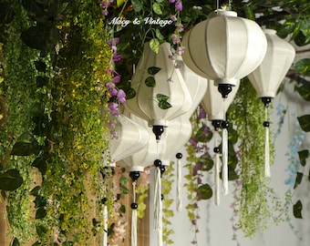 May include: White silk lanterns with black tassels hanging from a branch with green leaves and purple flowers. The lanterns are round and have a pleated design. The text "Macy & Vintage" is visible in the image.