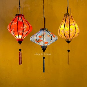 May include: Three hanging paper lanterns with floral patterns. The lanterns are red, blue, and yellow with black trim. The lanterns are hanging from black cords with tassels.