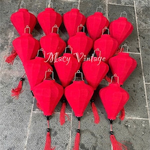 May include: A collection of red paper lanterns with black accents and tassels. The lanterns are arranged in a group, with the text "Macy Vintage" in the center. The lanterns are a traditional decorative item.