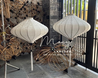 May include: Two white fabric lanterns with a white tassel hanging from the bottom. The lanterns are hanging from the ceiling and are in front of a wooden fence.
