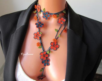 May include: A floral necklace with a cascading design. The necklace features orange and blue flowers with green leaves, set against a dark blue background. The necklace is displayed on a mannequin wearing a black blazer.