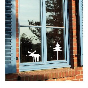 May include: A blue window with white shutters. The window is decorated with a white moose and a white pine tree cutout.