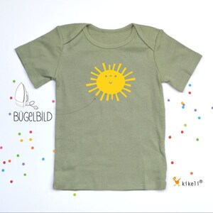 Könnte beinhalten: Hellgrünes Baby-T-Shirt mit gelbem, lächelndem Sonnensymbol. Das Shirt hat kurze Ärmel und einen Rundhalsausschnitt. Der Text "BÜGELBILD" ist ebenfalls sichtbar.