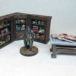 Könnte beinhalten: Ein Miniatur-Tischset für Rollenspiele, bestehend aus einem Holztisch mit einem Skelett, einem Holzschrank mit Regalen voller Bücher und Tränke sowie einer Miniaturfigur eines Zauberers mit einem Schwert.
