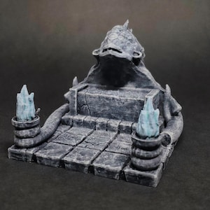 May include: A gray, fantasy-themed miniature altar with a textured surface. The altar features a tiered base, a central platform, and a sculpted top. Two blue flame-like structures flank the altar, adding a mystical element.
