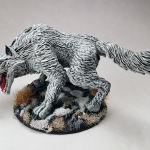 May include: A white wolf figurine with a snarling expression, painted with realistic details. The wolf is standing on a round base with brown and white textured grass.