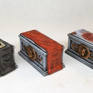 May include: Three miniature coffins with detailed designs. One has a skeleton, another a red cloth, and the third has a blood-like pattern. Each coffin features a skull emblem and decorative trim, perfect for Halloween or gothic decor.