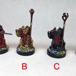 Puede incluir: Cuatro figuras en miniatura pintadas de figuras esqueléticas que llevan túnicas y sostienen bastones. Las figuras están pintadas en diferentes colores, incluyendo rojo, negro, dorado y marrón. Las figuras están de pie sobre bases circulares.