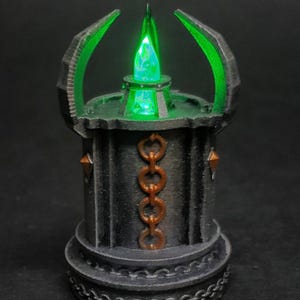 May include: A black and green 3D printed miniature of a glowing crystal on a pedestal with a chain design.