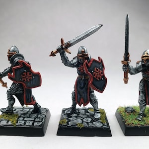 May include: Three miniature knight figurines, each posed with a sword and shield. The knights wear silver armor with black and red accents. Their shields feature a red cross design. The bases are textured to resemble stone or grass.