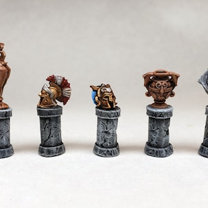 Può includere: Cinque colonne in pietra in miniatura con diverse cime decorative. Le cime includono un vaso di bronzo, un elmo di bronzo, un busto di bronzo, un elmo d'oro e un vaso d'oro.
