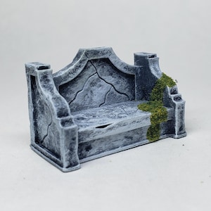 May include: A miniature, weathered stone bench, painted in shades of gray with visible cracks and a touch of green moss. The bench has a curved back and a rectangular seat, perfect for tabletop gaming or miniature displays.