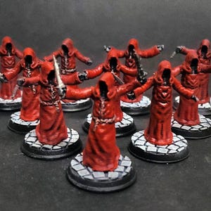 May include: Miniature figures of robed characters in red with hoods, each holding a sword. The figures stand on circular bases with a cobblestone pattern. The figures are arranged on a dark surface.