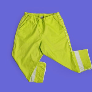 May include: Bright lime green trousers with white stripes down the sides. The trousers have a drawstring waist and pockets. Made from a lightweight material, suitable for casual wear.