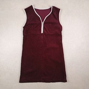 Può includere: Abito senza maniche bordeaux con motivo a pois bianchi. L'abito presenta un bordo bianco intorno allo scollo e alle ascelle e una cerniera bianca sul davanti. L'abito è un design semplice ma elegante.