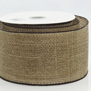 May include: A wide spool of natural tan burlap ribbon featuring a coarse, woven texture and dark brown stitched edges. The ribbon is wound tightly around a white circular cardboard core, displaying a consistent, neutral earthy tone throughout.