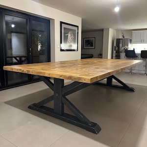 May include: A large wooden dining table with a rustic, natural finish. The table has a thick, rectangular top and a black, X-shaped base.