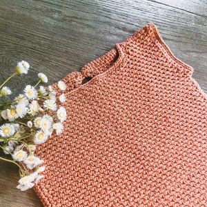 May include: A crocheted sleeveless top in a terracotta color. The top has a round neckline and a delicate crocheted pattern.