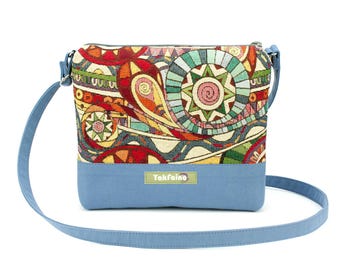 May include: A blue crossbody bag with a colorful patterned flap featuring geometric shapes and swirls. The bag has a blue strap and a label that reads "Yakfaino".
