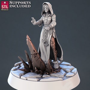Puede incluir: Miniatura impresa en 3D de una figura con túnica y antifaz, sosteniendo un báculo. La figura está sobre una base rocosa con una gran formación de cristal marrón oscuro. El texto "SUPPORTS INCLUDED" y "STL Miniatures" es visible.