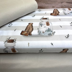 Könnte beinhalten: Drei Stoffstücke, eines mit einem weißen und grauen Streifenmuster mit Bären und Glasbehältern mit dem Wort "Abenteuer" darauf, eines in einfarbiger grauer Farbe und eines in einfarbiger beige Farbe.