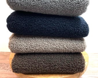 May include: A stack of four plush fabric swatches in different colors: gray, navy blue, light brown, and dark brown. The swatches are stacked on a wooden stand.
