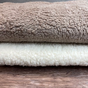 May include: Two pieces of fluffy fabric, one beige and one white, are folded and stacked on top of each other. The fabric is soft and plush, with a fuzzy texture.
