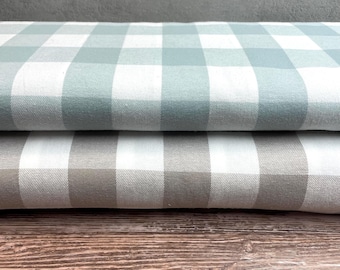 May include: Two stacks of fabric with a classic buffalo check pattern. The top layer features a light blue and white checkered design, while the bottom layer displays a gray and white checkered pattern. The fabric is folded neatly, suggesting it's ready for use in sewing or crafting projects.