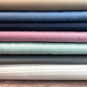 May include: A stack of eight different colored ribbed fabrics. The fabrics are arranged in a vertical stack, with the top fabric being a light brown color. The fabrics are all ribbed and have a soft, textured feel.