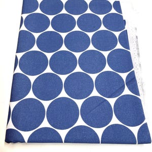 Könnte beinhalten: Gefalteter Stoff mit einem sich wiederholenden Muster aus großen, marineblauen Kreisen auf weißem Hintergrund. Der Stoff ist einfarbig und scheint aus Baumwolle oder einem ähnlichen Material zu sein. Die Kanten des Stoffes sind sichtbar und zeigen die geschnittenen und gefalteten Schichten.