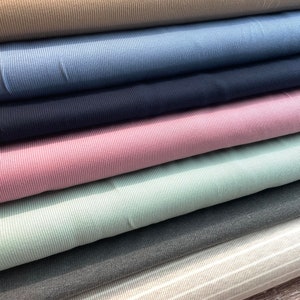 May include: A stack of seven different colored ribbed fabrics. The fabrics are arranged from top to bottom in the following order: beige, blue, navy, pink, light green, gray, and white with gray stripes.