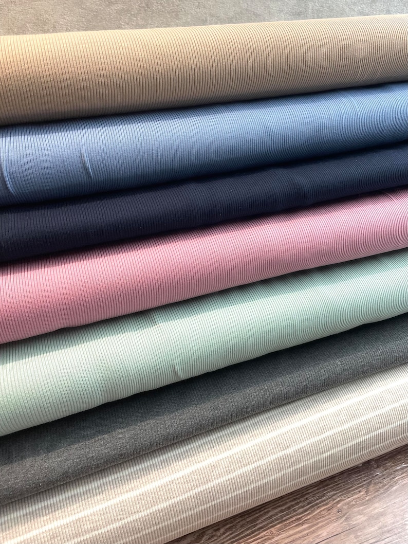 May include: A stack of seven different colored ribbed fabrics. The fabrics are arranged from top to bottom in the following order: beige, blue, navy, pink, light green, gray, and white with gray stripes.