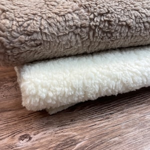 May include: Two pieces of fluffy faux fur fabric. One is a light brown color and the other is white. The fabric is folded and placed on a wooden surface.