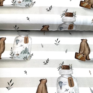 Könnte beinhalten: Ein weiß-beiger gestreifter Stoff mit einem sich wiederholenden Muster aus Bären, Glasflaschen und Grünpflanzen. Die Flaschen sind mit einer blauen Flüssigkeit gefüllt und enthalten ein kleines Segelboot, einen Heißluftballon und ein Flugzeug. Die Bären sind braun und tragen Koffer mit der Aufschrift "Hello World". Die Flaschen haben Etiketten mit der Aufschrift "Adventure".