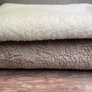 May include: Two folded blankets, one white and one brown, are stacked on top of each other on a wooden surface.