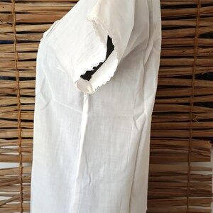 May include: A white, short-sleeved blouse with delicate lace trim along the neckline and sleeve edges. The blouse is made of a lightweight fabric and has a simple, classic design. The garment is displayed on a black mannequin.