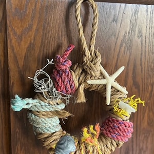 May include: A natural fiber wreath decorated with seashells, starfish, and rope. The wreath is a light brown color and has a rustic look.