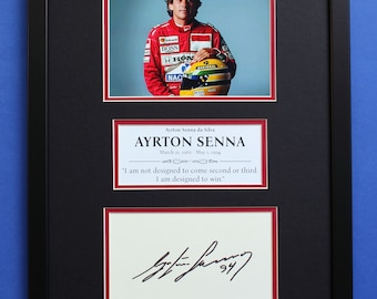 May include: Framed print featuring Ayrton Senna. The top section shows a photo of Senna in a red racing suit, holding a helmet. Below, a text panel reads "AYRTON SENNA" with his birth and death dates, and a quote. The bottom section displays a signature.